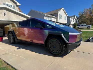Futuristic Tesla Cybertruck with iridescent paint parked in a suburban driveway.