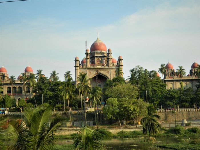 Historic building with red domes surrounded by greenery under a clear sky.