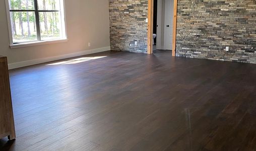 A large bedroom with dark hardwood flooring and stone walls with bright sunshine into the windows ha