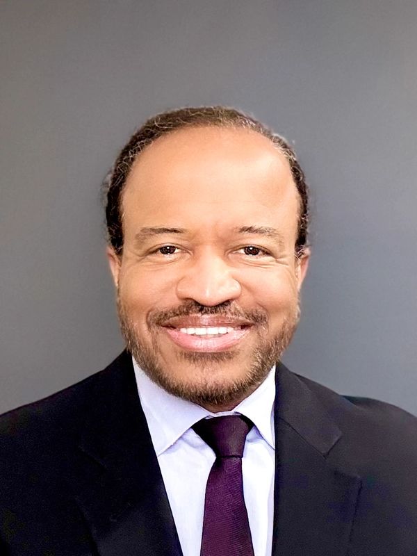 Smiling man in formal suit and tie against a plain background.