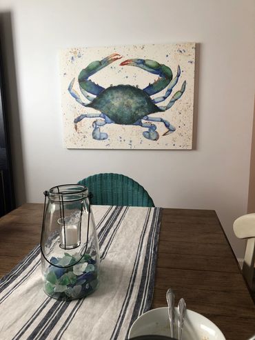 Canvas blue crab watercolor art hanging on interior wall in beach home in dining room.
