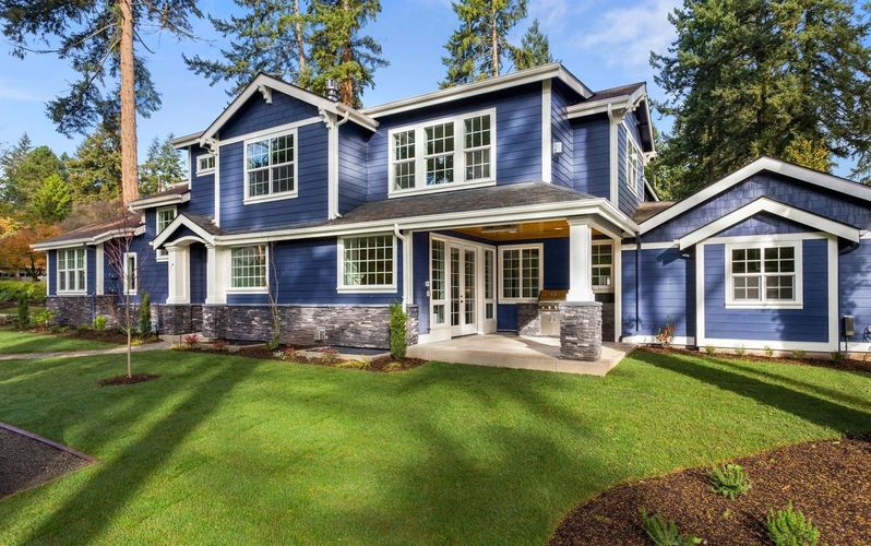 Facade of Home With Manicured Lawn, and Backdrop of Trees and Blue Sky