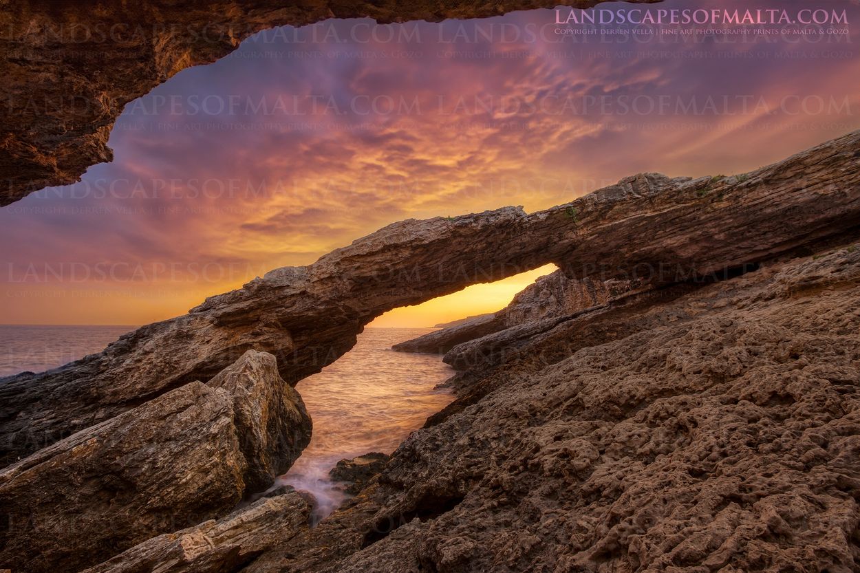 colours of gozo with a dramatic and colorful sunset photographed from a natural sea arch in Qala