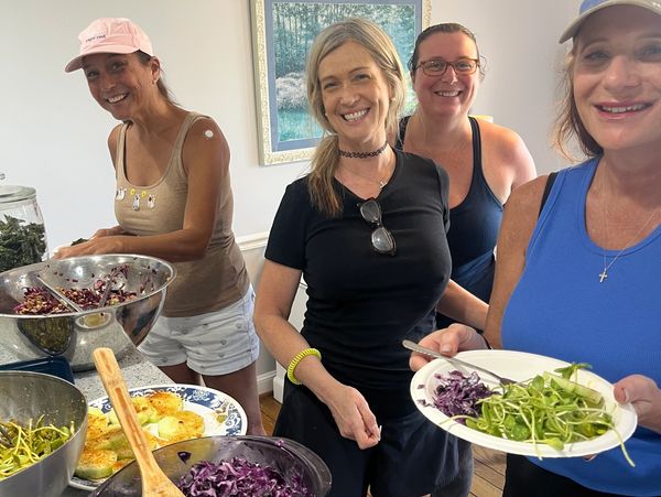 Four women smiling while preparing and serving salad.