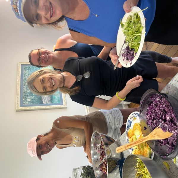 Four women smiling while preparing and serving salad.