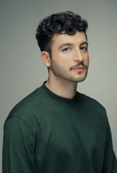 Homem jovem com cabelo encaracolado e camiseta verde.