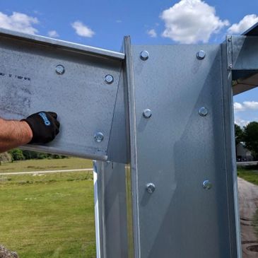 A worker's gloved hand bolting metal beams outdoors under a blue sky.