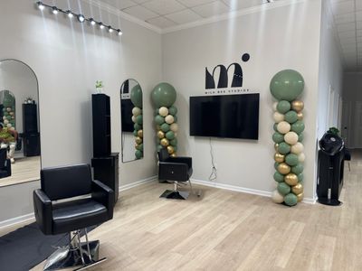 Modern beauty salon with black chairs, mirrors, and balloon decorations.