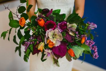 Spring bridal bouquet with tulips, ranunculus, ornamental kale, and lilac in bold orange and purple.