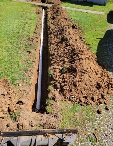 Trench with a newly installed white PVC pipe in a grassy area.