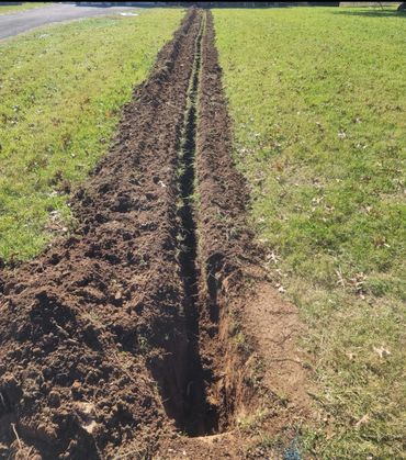 Freshly dug trench in a grassy area under sunlight.