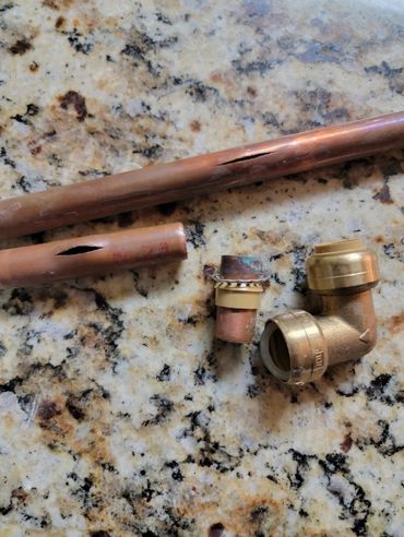 Damaged copper pipes and plumbing fittings on a granite surface.