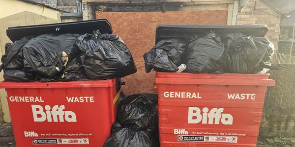 Two red Biffa general waste bins overflowing with black garbage bags.