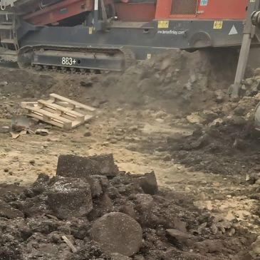A large red construction machine working on rocky soil outdoors.