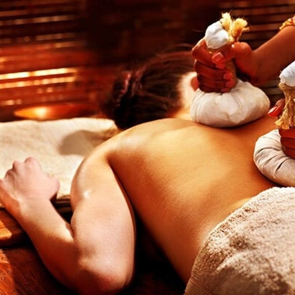 Person receiving a herbal compress massage on their back in a spa.