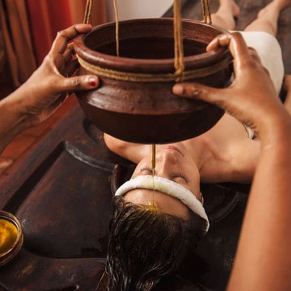 Person receiving Ayurvedic Shirodhara therapy with oil dripping on forehead.