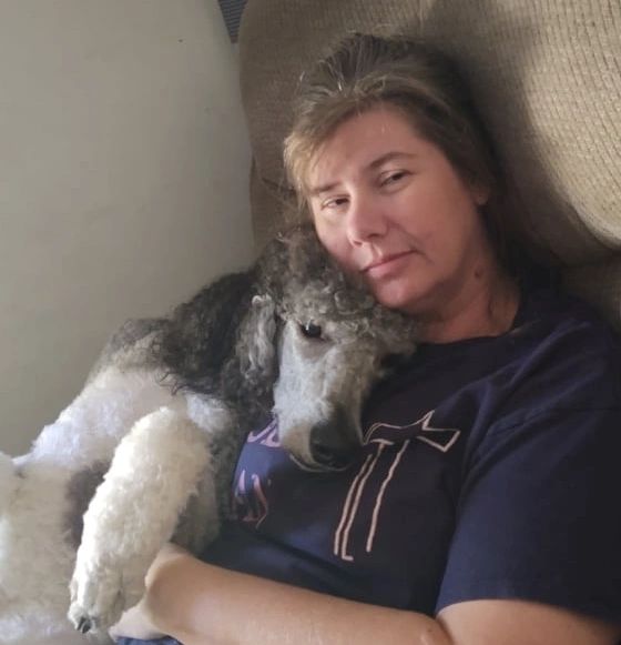a white woman sitting cuddling a standard poodle puppy