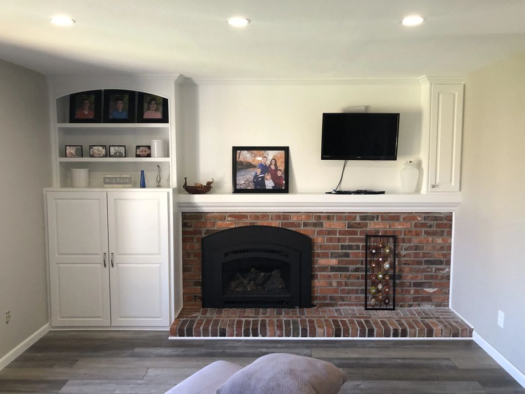 Finished mantel wall with white built-in cabinets around a brick fireplace