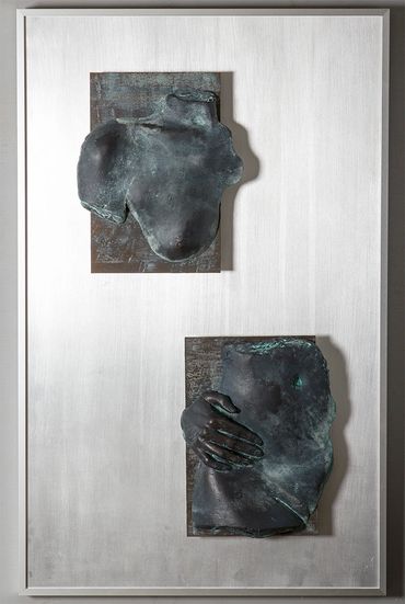 2 cast bronze sculptures of female body parts mounted to metal board, creating an image of a figure