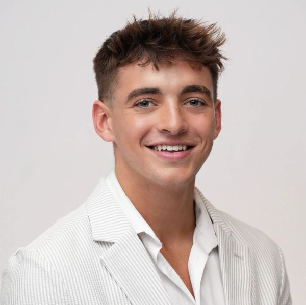 Young man smiling in white suit jacket.