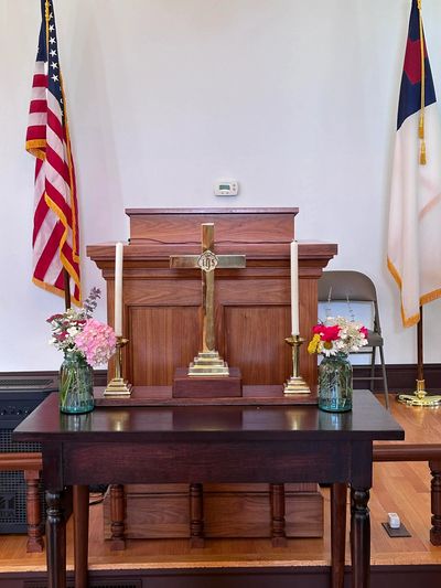 Church altar with cross, candles, flowers, and flags in the background.