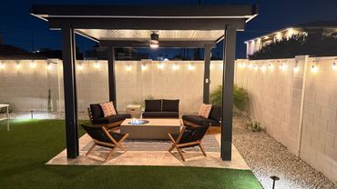 Cozy outdoor seating area with a fire pit under a pergola and string lights at night.