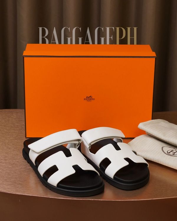 Hermes white leather sandals with black soles in front of an orange Hermes box.