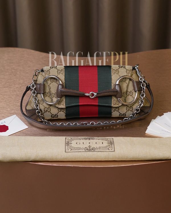 Gucci handbag with signature GG pattern and red-green stripe on a table.