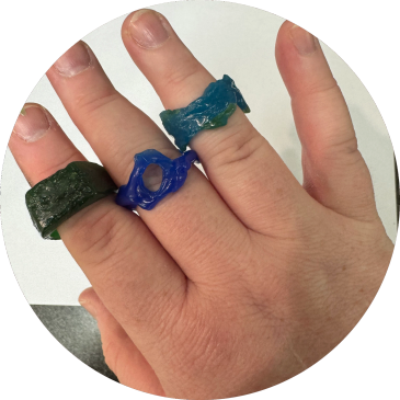 Hand with three colorful resin rings on fingers.