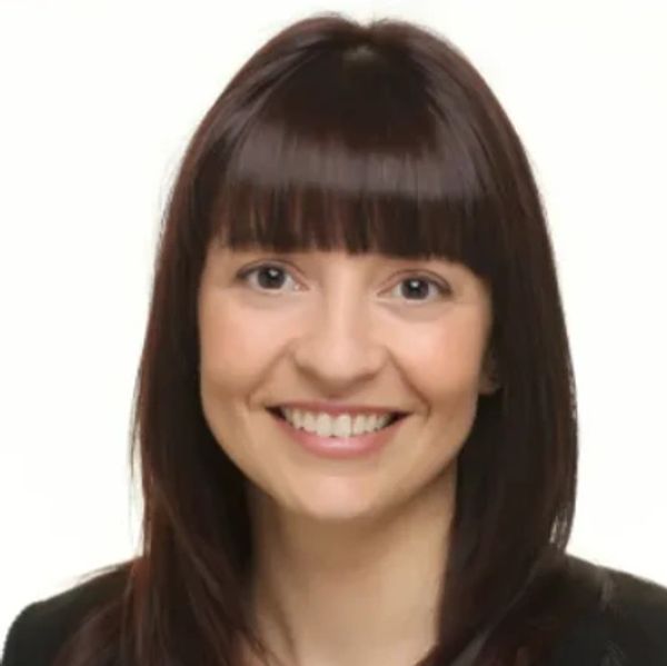 Smiling woman with straight brown hair and bangs against a plain background.