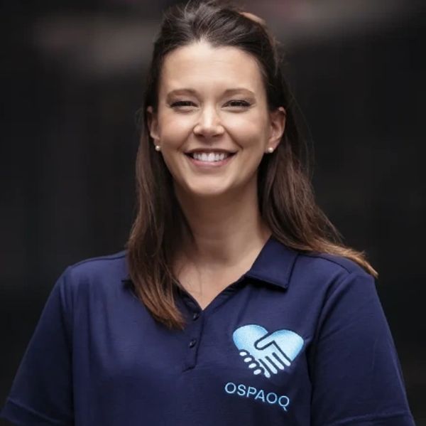 Smiling woman in a blue polo shirt with a handshake heart logo.