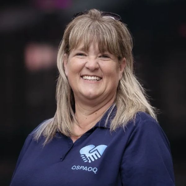 Smiling woman in a navy polo shirt with a handshake logo.