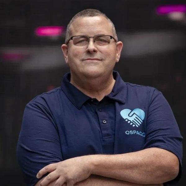 Man in glasses and navy polo shirt with a handshake heart logo.