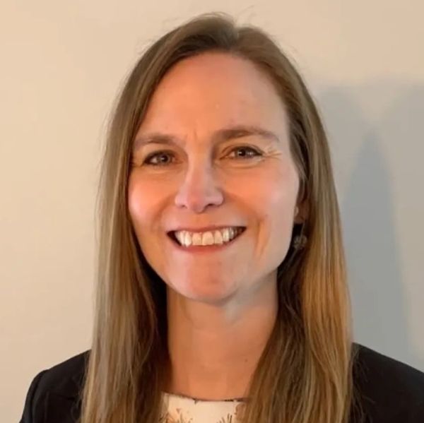 Smiling woman with long brown hair in formal attire against a plain background.
