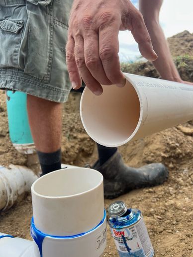 Worker connecting PVC pipes with glue outdoors.