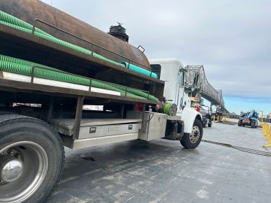 Side view of a utility truck with coiled green hoses and equipment on a construction site.