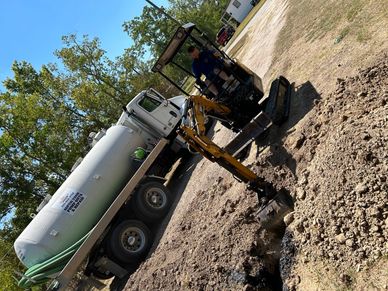 Mini excavator working beside a large septic tank truck.
