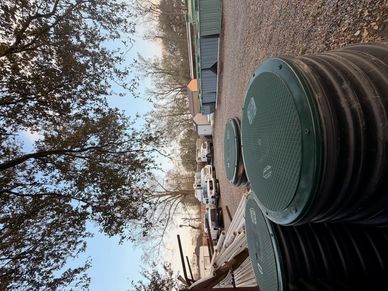 Large green plastic barrels stacked outdoors near trees and cars.