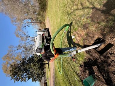 Worker clearing a septic tank with hose and truck.
