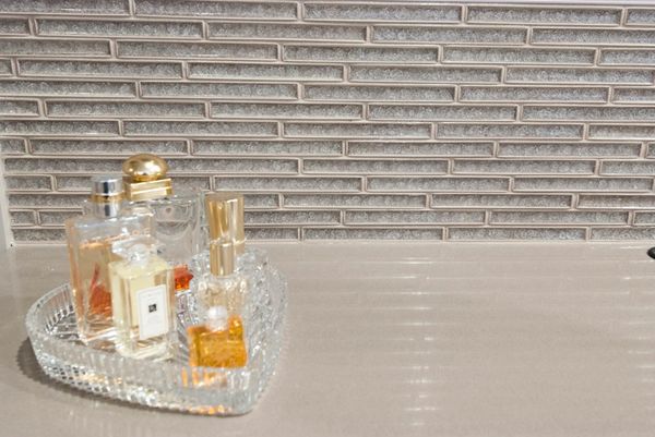Perfume bottles arranged on a heart-shaped glass tray against a tiled wall.