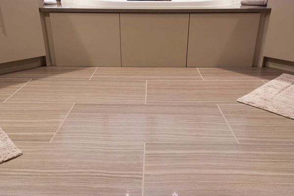 Modern bathroom floor with beige tiles and matching rugs.