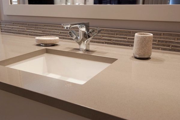 Modern bathroom sink with beige countertop and chrome faucet.