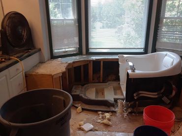 Partially removed bathtub in a bathroom under renovation with tools and debris around.