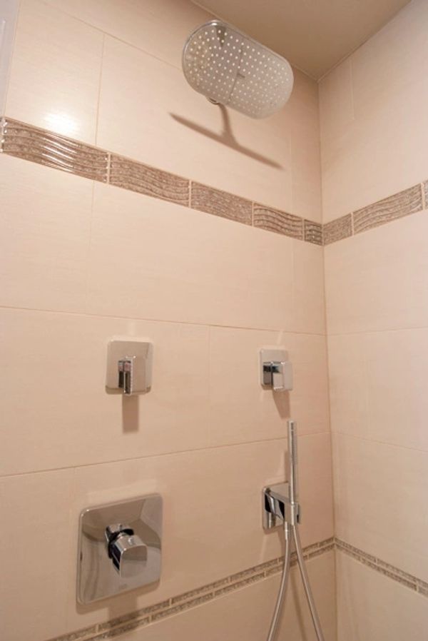 Modern shower setup with square chrome fixtures and beige tiled walls.