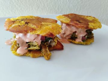 Two tostones sandwiches with shredded meat and sauce on a white plate.