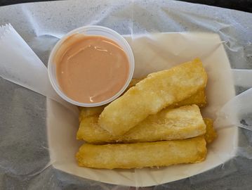 Fried yuca sticks served with a creamy dipping sauce in a paper-lined tray.
