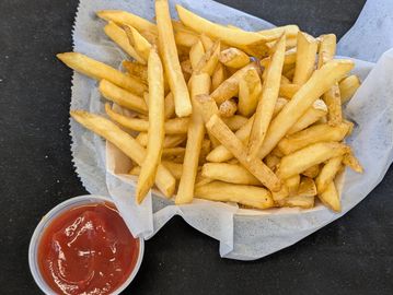 Golden French fries served with a side of ketchup on a black surface.