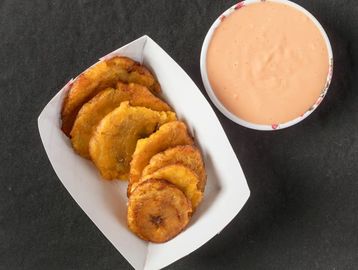 Fried plantains served with a creamy dipping sauce on a black background.