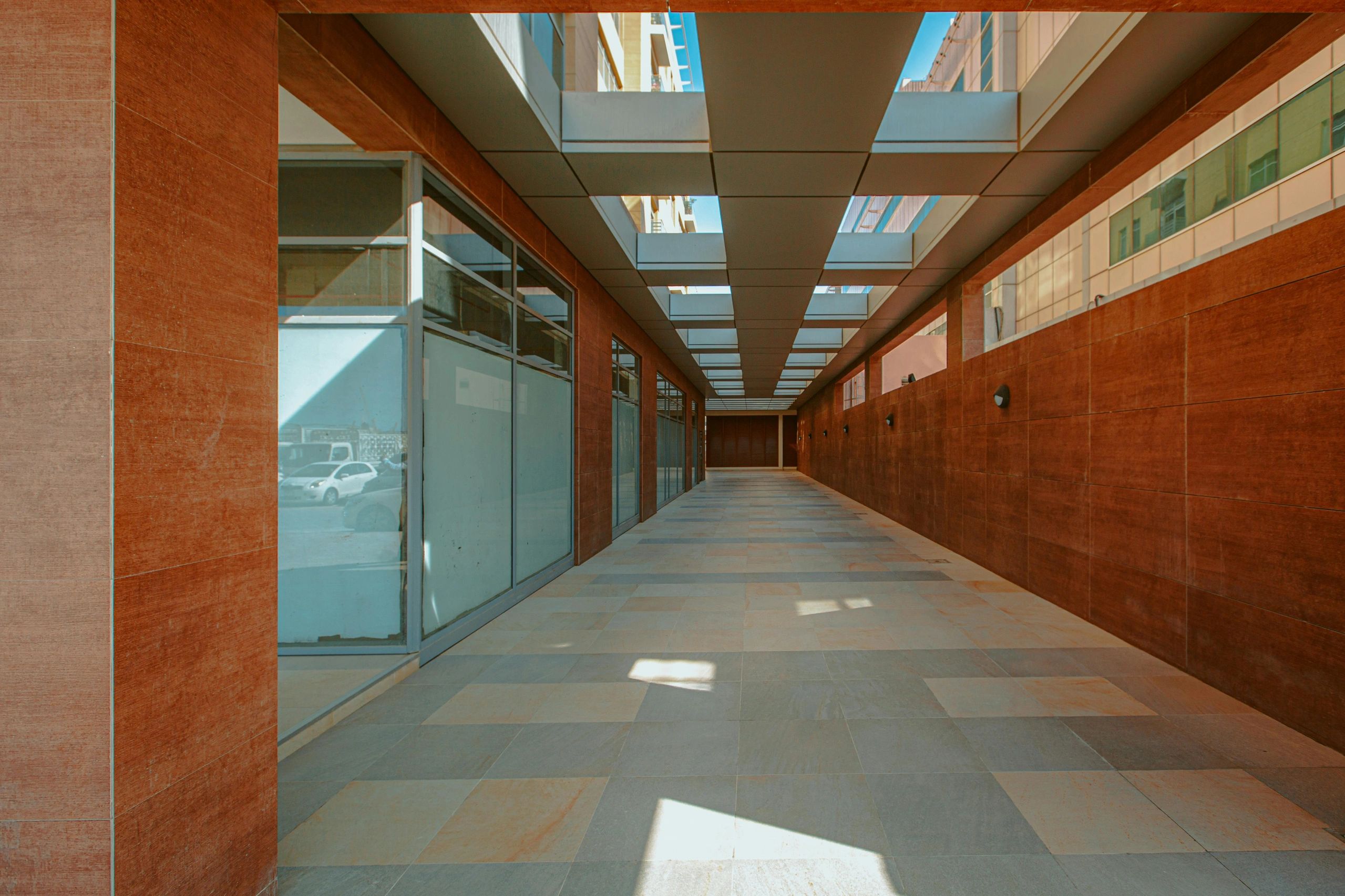 Modern corridor with glass windows and tiled walls under a ceiling with rectangular openings.