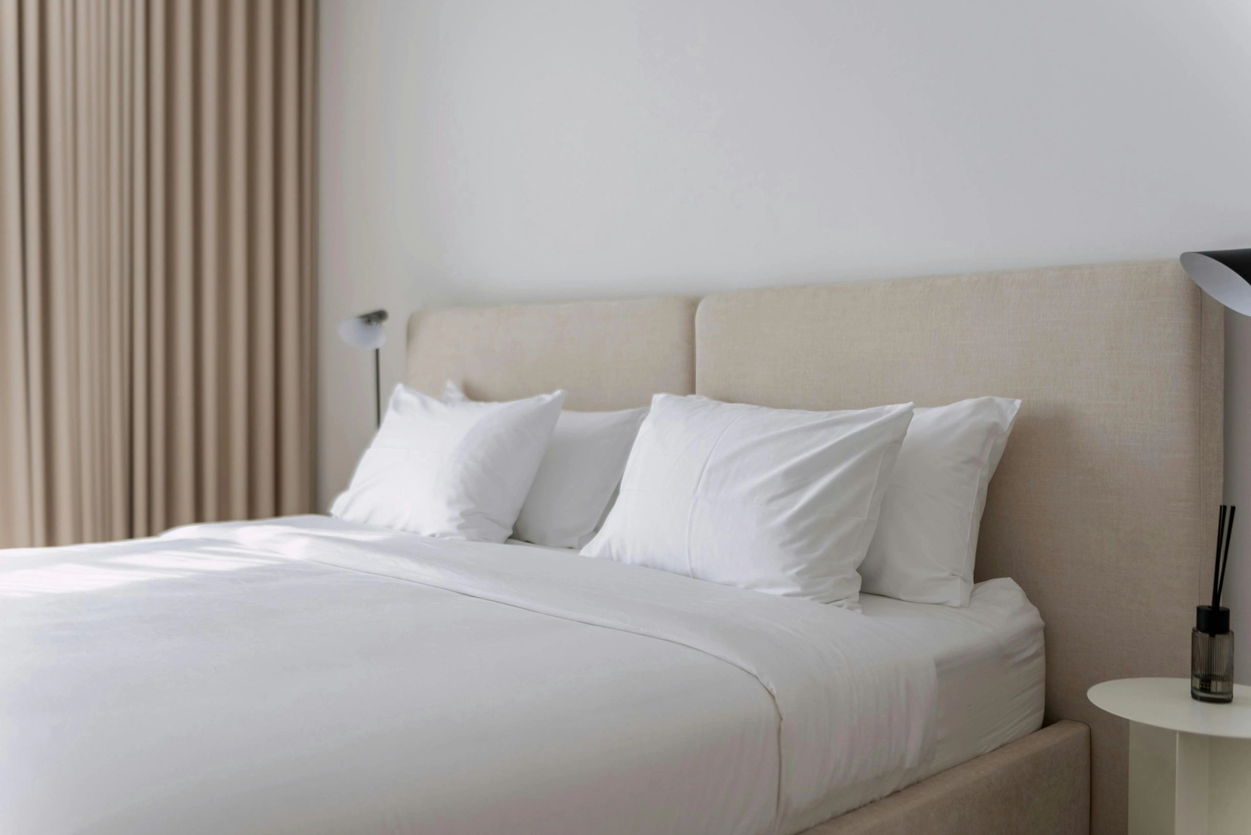 Minimalist bedroom with beige headboard and white bedding.
